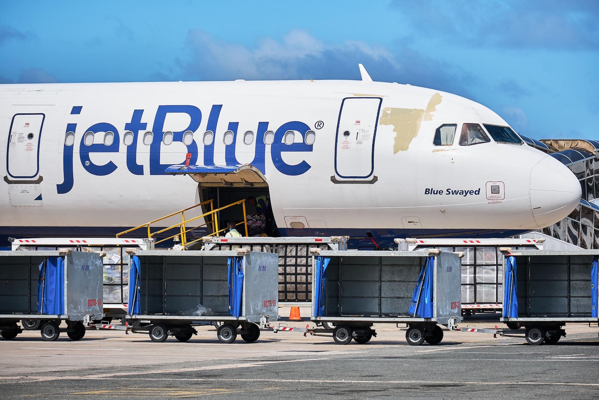 JetBlue aircraft loading bags with blue skies behind it